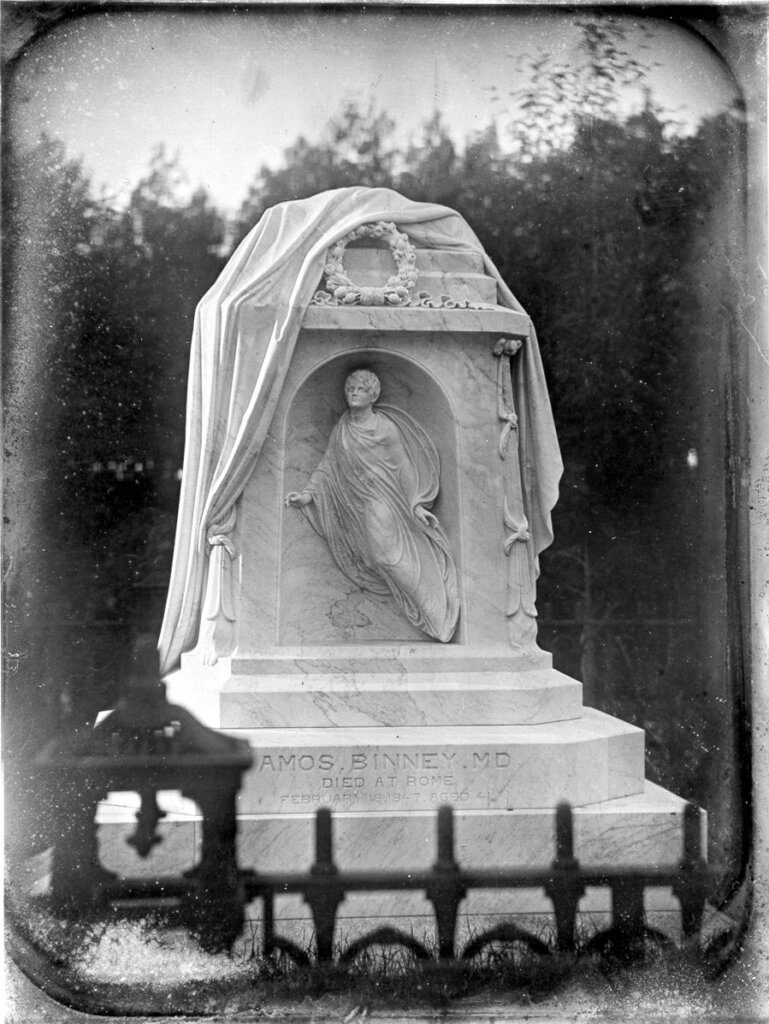 An historic photograph of a cemetery monument with a shroud draped over an angel sculpted. 