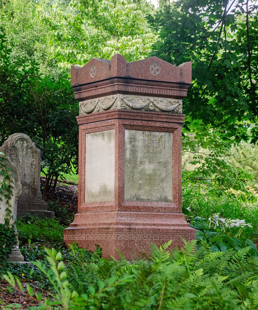 A rectangular monument in a cemetery surrounded by ferns