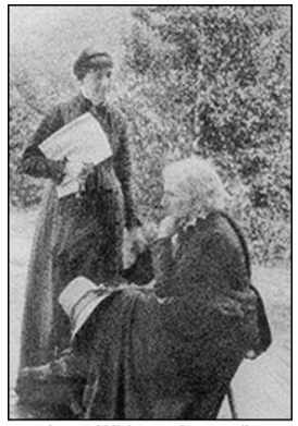 An historic photograph of two women. One seated, one standing. 