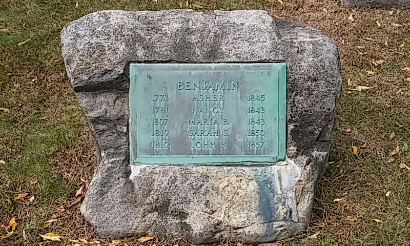 a stone gravestone memorial with a bronze plaque in the center