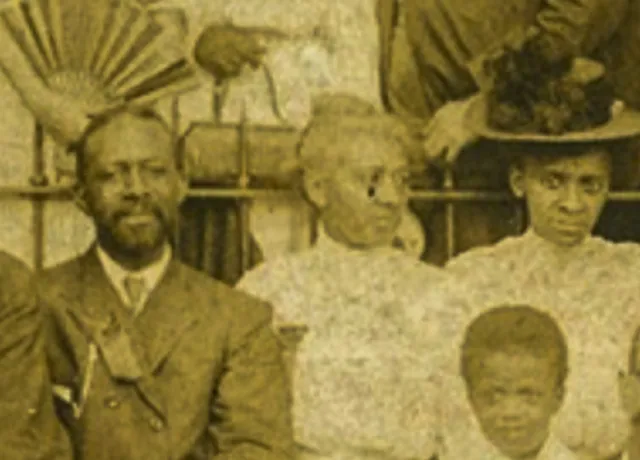 An historic photograph in sepia of two Black woman, one Black man, and a Black child