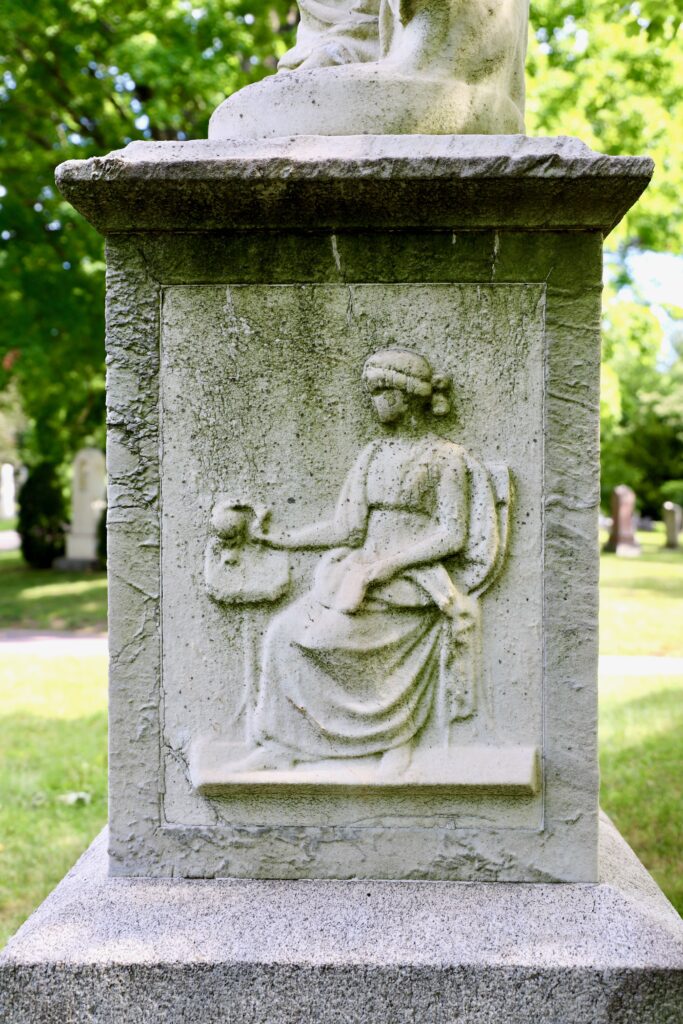 A close-up photograph of relief carving of a woman seated on a funerary monument
