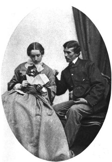 An historic photograph of a young couple, seated, and reading a book. 