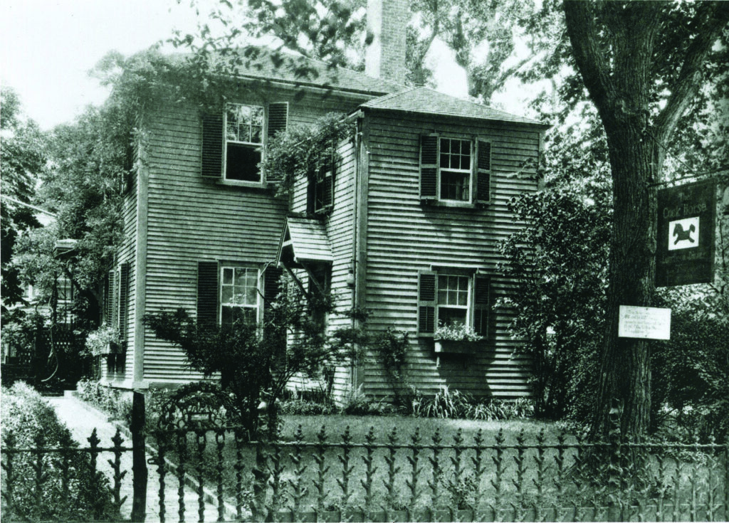 An historic photograph of a New-England-style house with a cast iron fence in the foreground. 