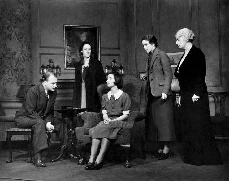 A 1930's film set with five actors. Three are standing, two are seated.