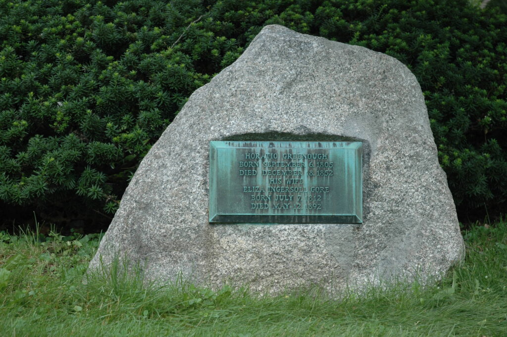 A photo of a boulder gravestone monument with a bronze plaque. 