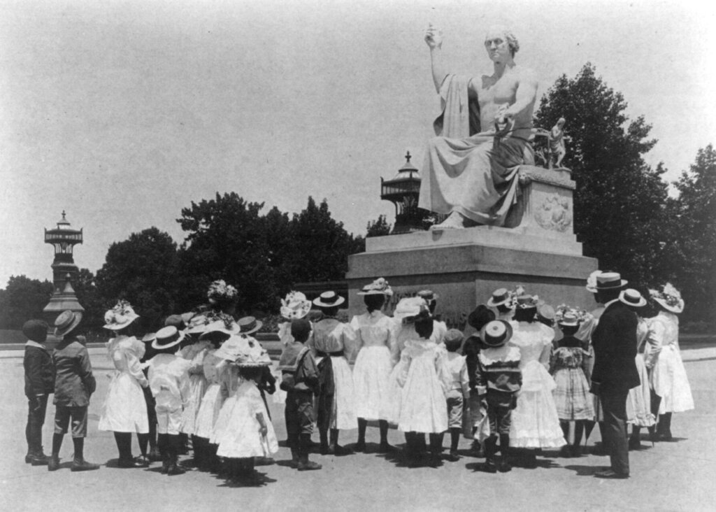 A group of school children standing below a statue of George Washington