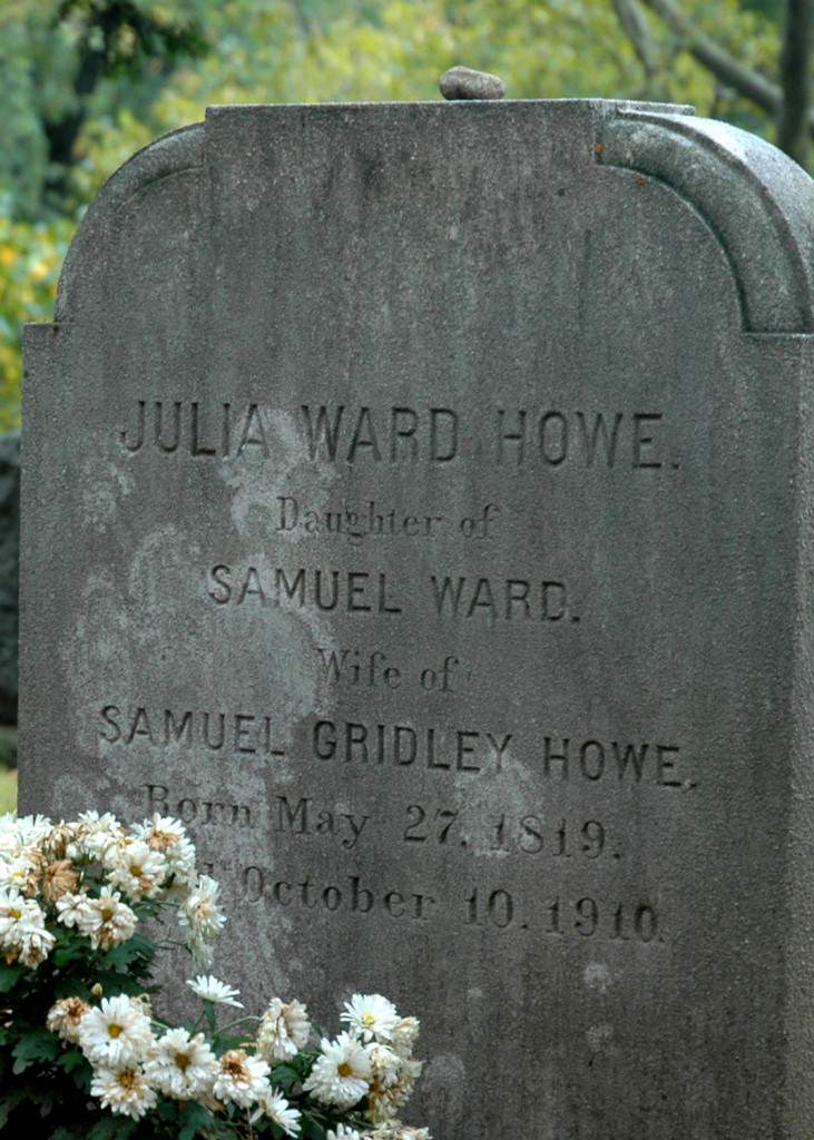 A close up photograph of a gravestone monument with small white flowers. 