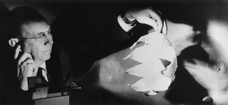 A black and white photograph of a man holding a balloon shattered by a bullet
