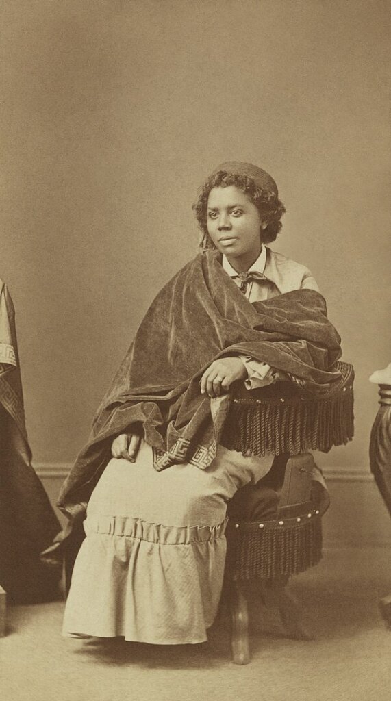A sepia image of a Black woman seated wearing a shall. 