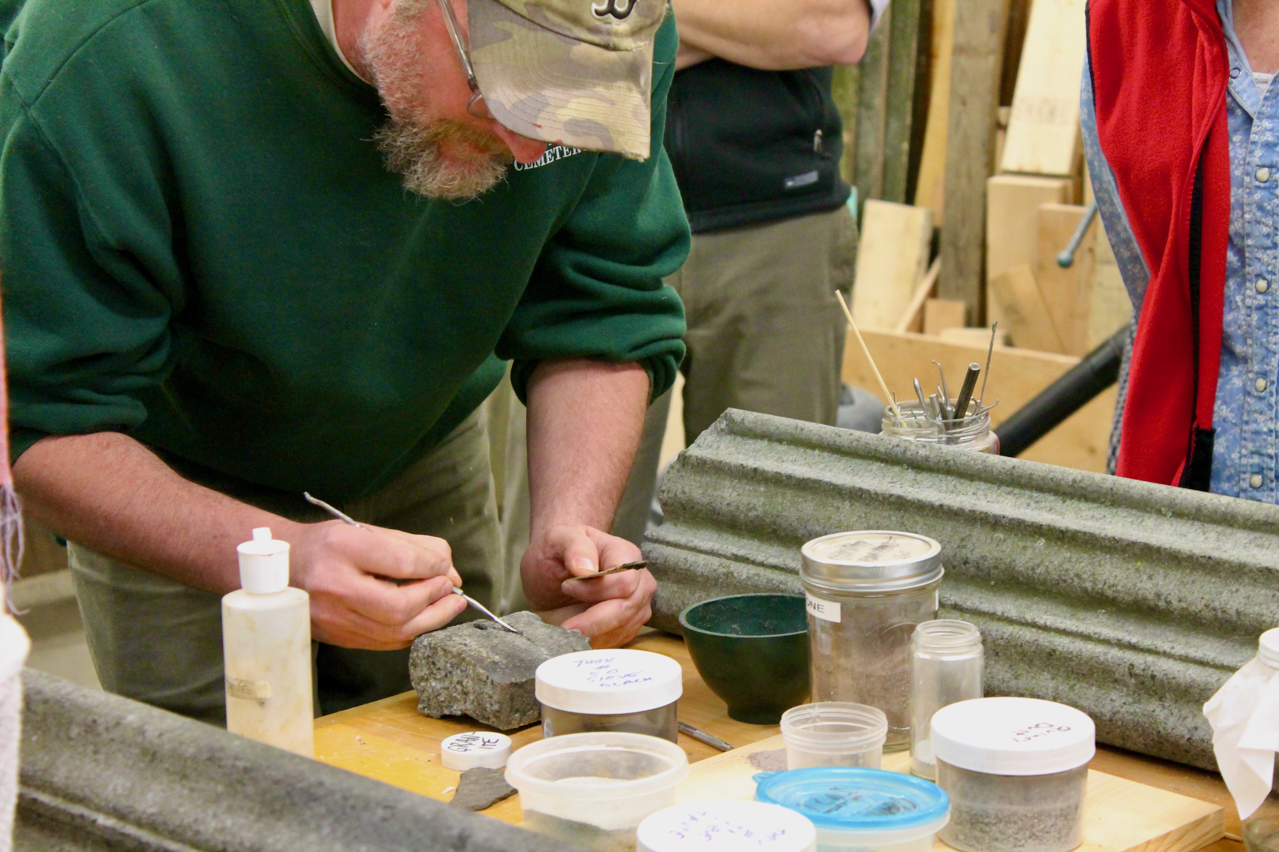 A man paints on a granite block surrounded by jars and mixing bowls