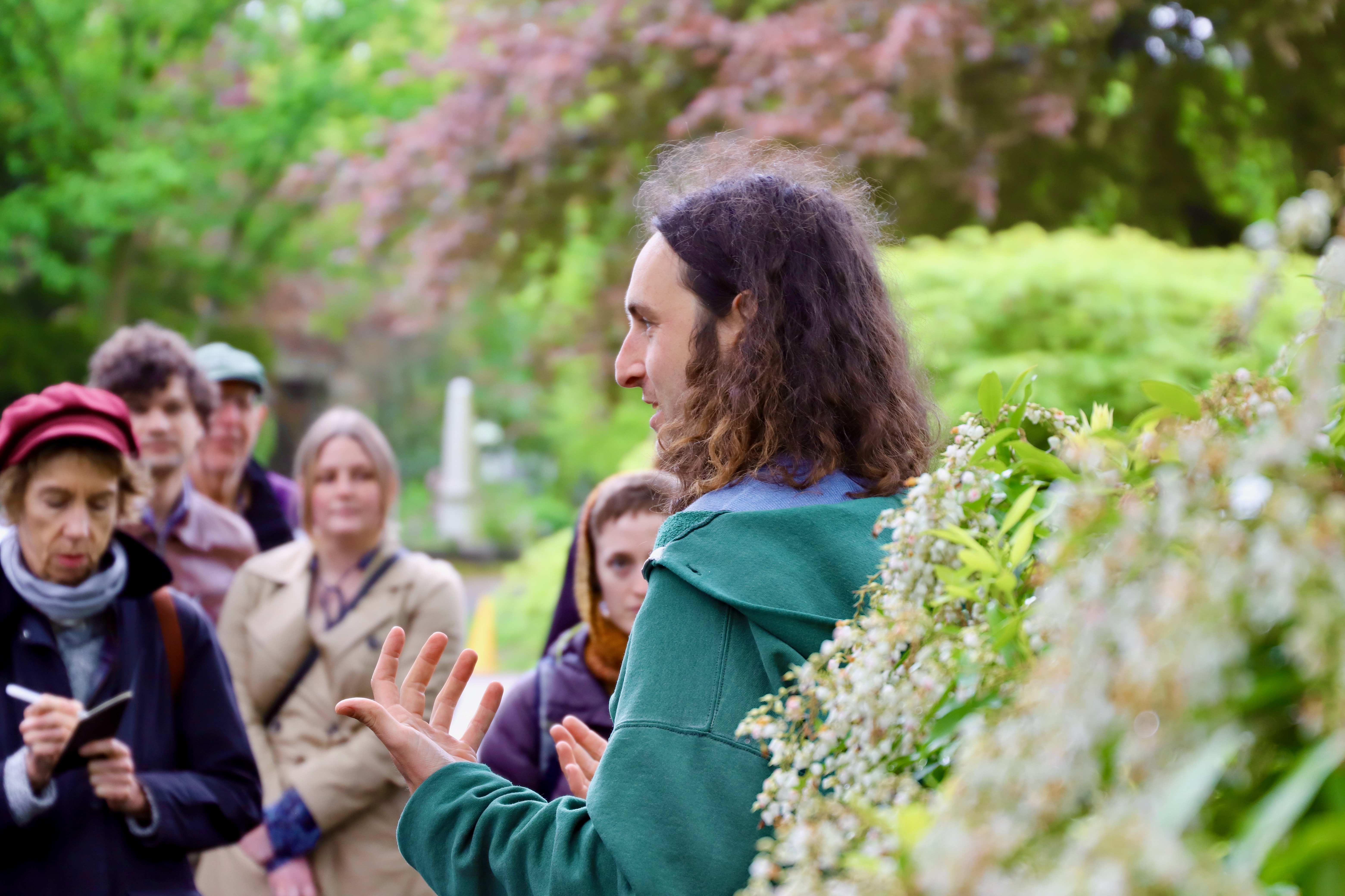 a man with curly hair speaks to a group of people taking notes.