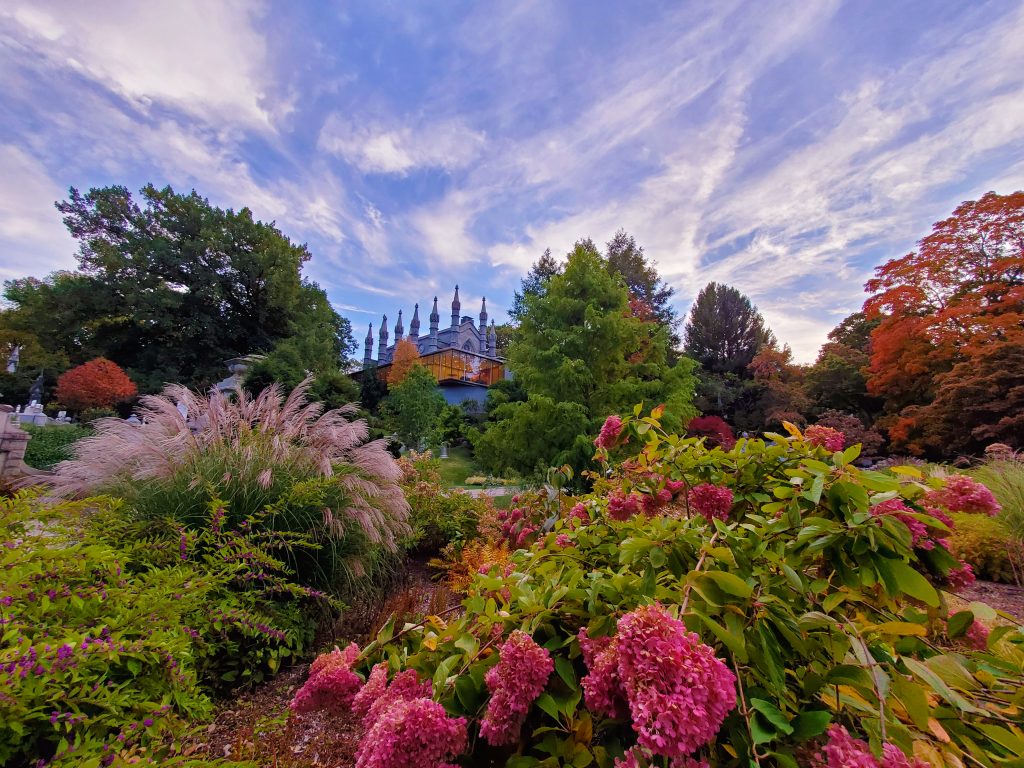 Color photograph with lush garden in the foreground, Bigelow Chapel in the distance, and the sky above.