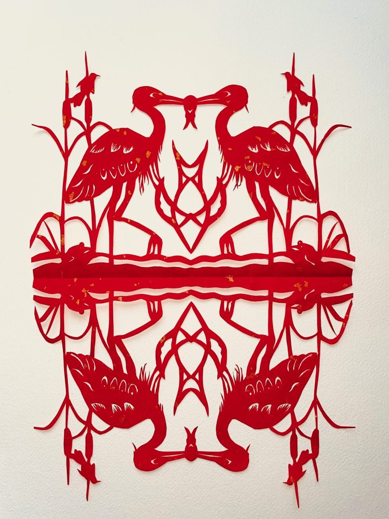 Red papercut artwork of birds sharing a fish